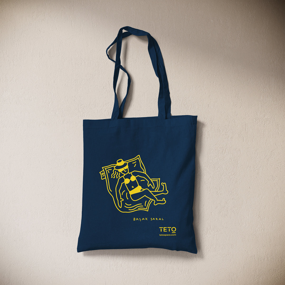 Tote bag in canvas Blu con illustrazione Pouf di Başak Saral (donna che prende il sole sdraiata sul pouf), vista frontale – TETO
