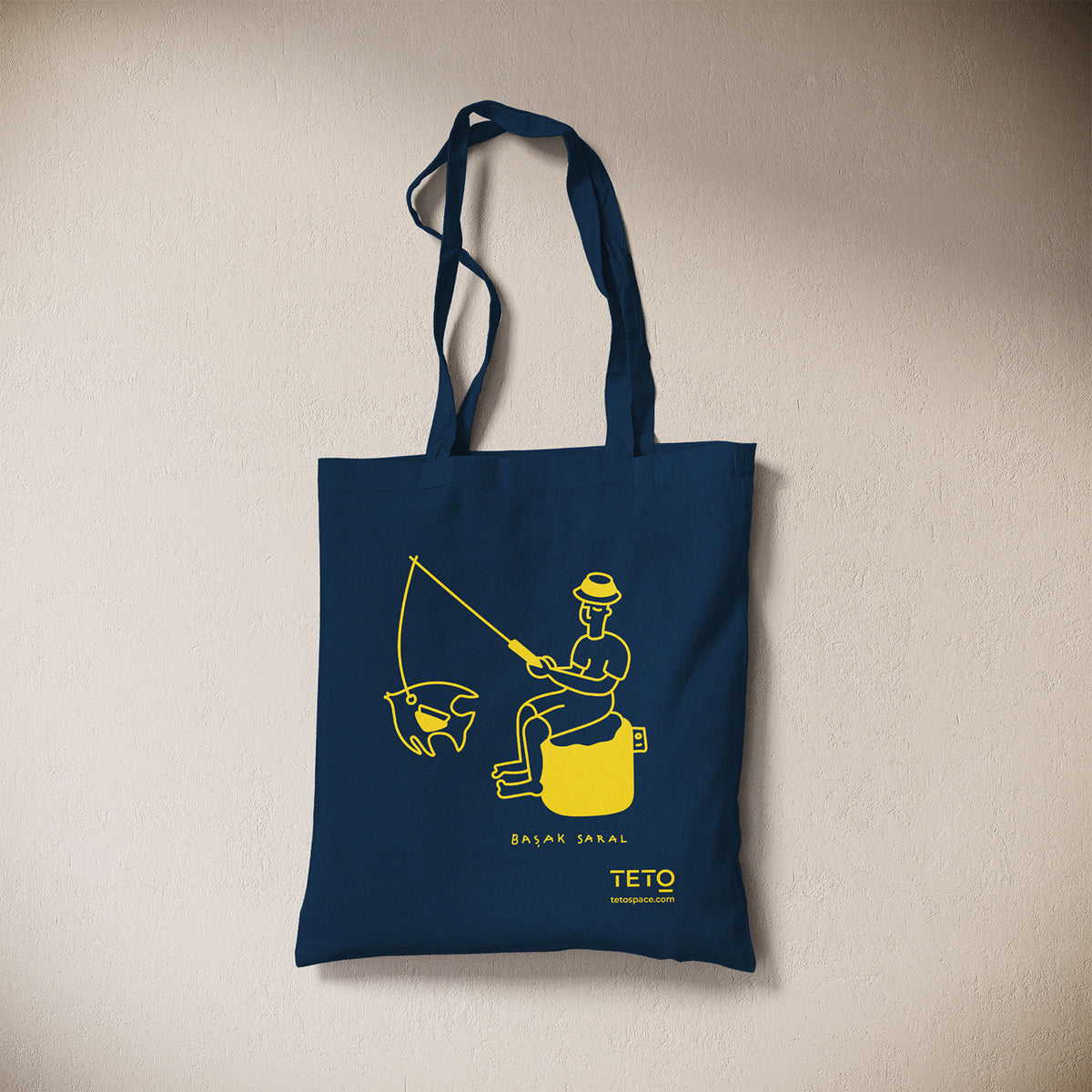 Tote bag in canvas Blu con illustrazione Fish di Başak Saral (pescatore seduto sul pouf), vista frontale – TETO