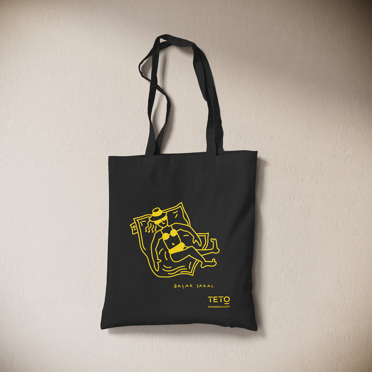 Tote bag in canvas Nero con illustrazione Pouf di Başak Saral (donna che prende il sole sdraiata sul pouf), vista frontale – TETO