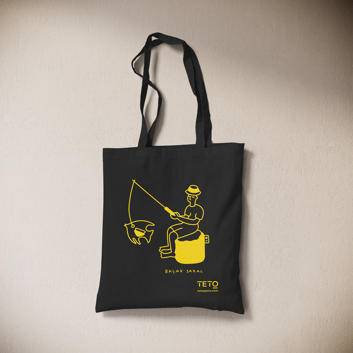 Tote bag in canvas Nero con illustrazione Fish di Başak Saral (pescatore seduto sul pouf), vista frontale – TETO