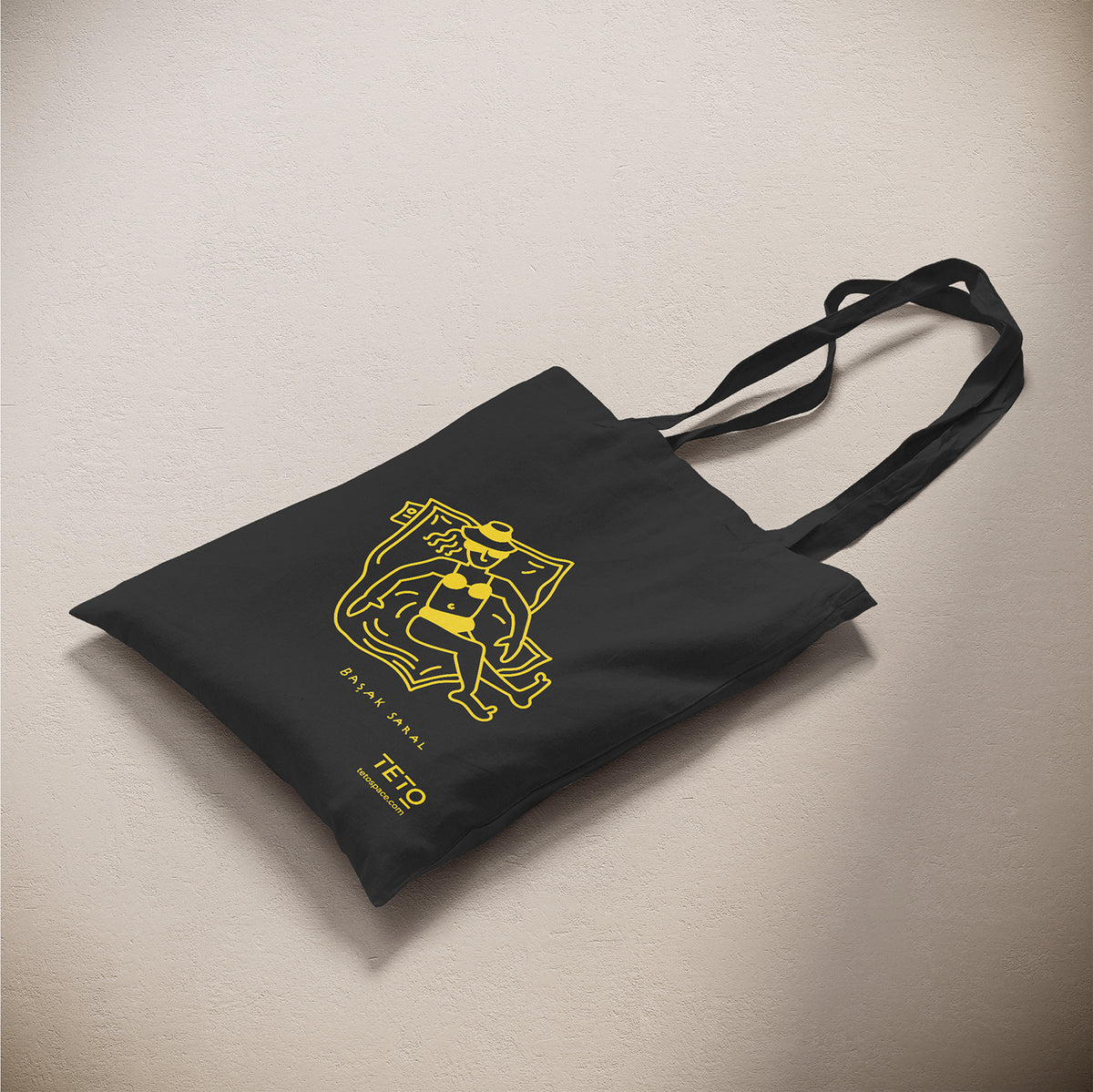 Tote bag in canvas Nero con illustrazione Pouf di Başak Saral (donna che prende il sole sdraiata sul pouf), vista laterale – TETO