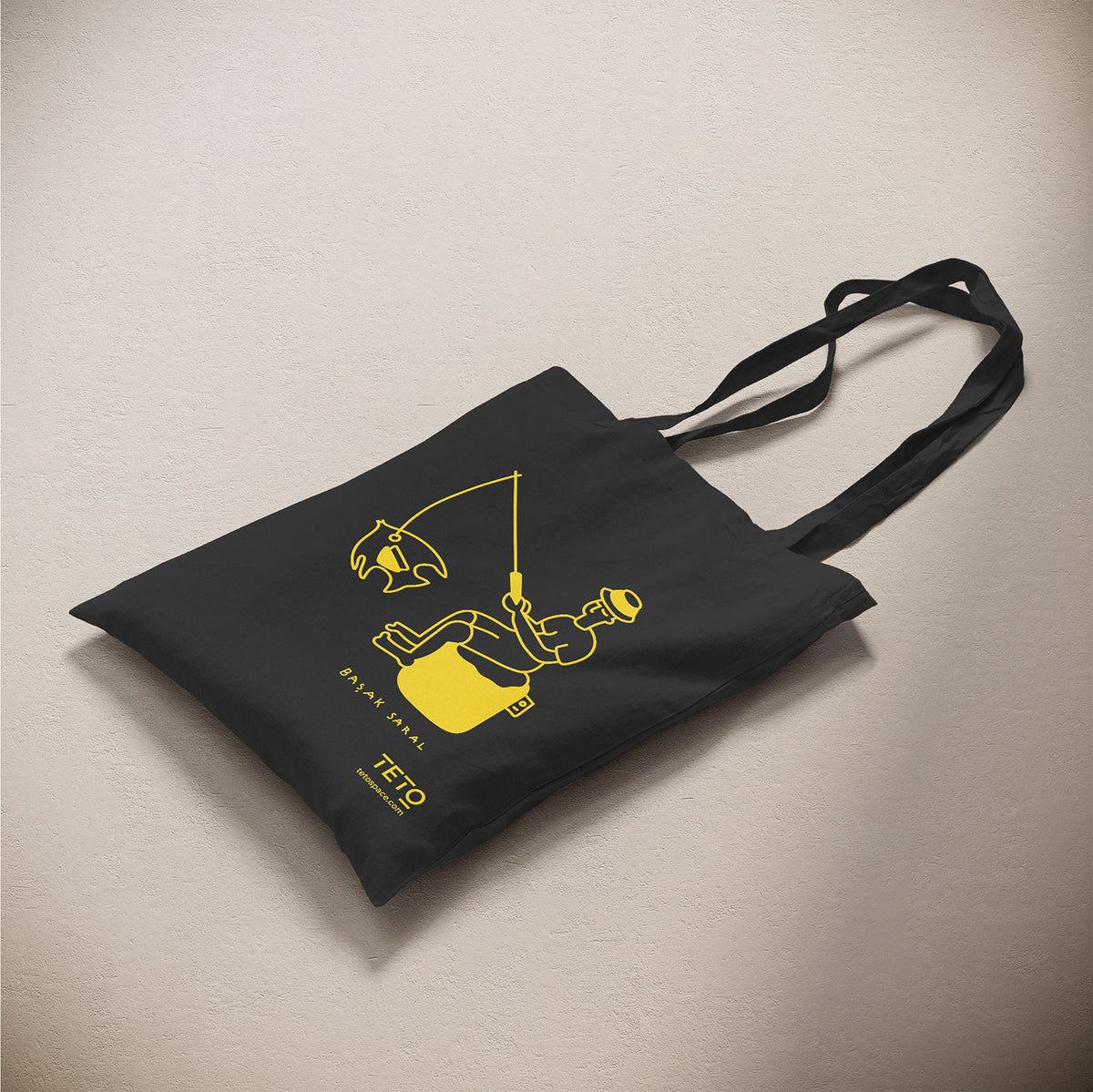 Tote bag in canvas Nero con illustrazione Fish di Başak Saral (pescatore seduto sul pouf), vista laterale – TETO